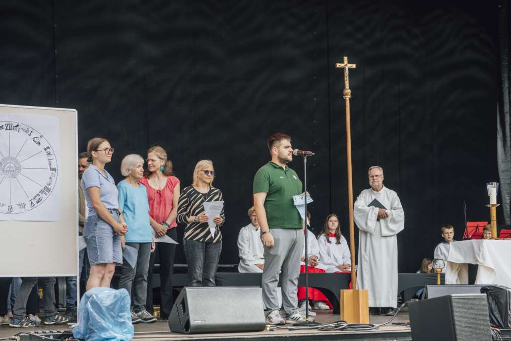 Gottesdienst_Close up Betreuer der Kinderfreizeit trägt eine Fürbitte vor. Gemeinsam mit dem Pfarrer und anderen Akteuren des Gottesdienstes auf der Bühne